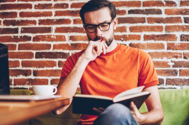 Akıllı hipster öğrenci ders kitabı hazırlama semineri için bilgilerin öğrenme konsantre. Coworking modern netbook ile masada oturan görev çalışmaya düşünme dalgın genç adam