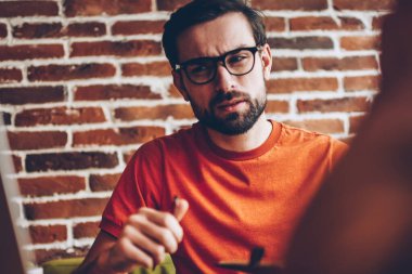 Şüpheci sakallı genç adam optik gözlük için 4 g bağlı modern dizüstü bilgisayar aygıt bakarak internet ve teknik sorun alanı iç coworking oturan düşünme