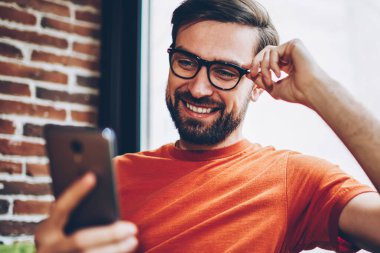 Güzel erkek blogger modern smartphone cep telefonu ile sosyal ağlarda arkadaşlarınızla sohbet ederken gülüyor sakallı. Cep video izlerken olumlu genç adam bağlı 4 g ücretsiz internet