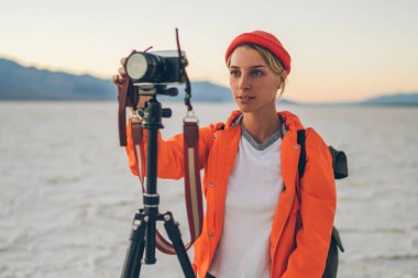ABD 'de Ölüm Vadisi' nde seyahat ederken, kuru arazide görkemli gökyüzünün fotoğrafını çeken, sırt çantalı, konsantre kadın gezgin.