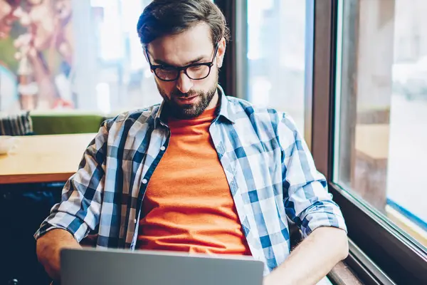 Dalgın sakallı erkek blogger gözlük sağlamak gözleri koruma online eğitsel dizüstü bilgisayar ile kablosuz internet izlemek için. Grafik tasarımcı netbook coworking içinde serbest çalışma