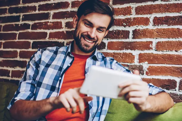 Mutlu sakallı genç adam modern Dokunmatik ped cihaz üzerinde Web sitesinde komik Haberler okuma rahat gömlek giymiş. Neşeli hipster blogger yayın 4 g internet bağlantısı üzerinden dijital tablet İndiriyor