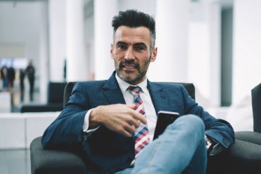 Formal giyim ofis iç dinlenme kendine güvenen olgunlaştı işadamı portresi giymiş. Akıllı gurur CEO'su 50 yaşında rahat koltukta otururken kameraya bakarak sakallı