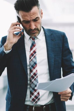 Muhasebe raporlarında mali sorunları çözmek için kendine güvenen gurur CEO'su formal giyim smartphone üzerinde arama içinde. Hareket eden telefon aygıt Office İç konuşurken elinde belgelerle ciddi iş adamı