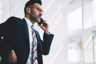 Kendine güvenen orta yaşlı Finans Müdürü smartphone üzerinde arama ve iş ortağı ile konuşurken formal giyim içinde. Gurur CEO'su pencereden dışarı bakarken telefon aygıtı üzerinde iletişim deneyimli