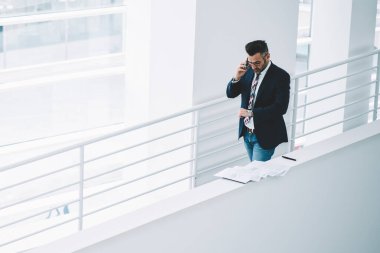 Üstten görünüm meşgul olgun işadamı toplantı ofiste zaman acele kontrol seyretmek bakarken smartphone üzerinde konuşuyor. Formal giyim hücresel cihaz arama orta yaşlı girişimci