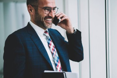 Pozitif olgun tüccar kıyafetli smartphone aygıt üzerinde iş ortağı ile telefon görüşmesi sırasında gülüyor. Cep üzerinde arama ve başarılı proje hakkında konuşmak neşeli gurur CEO'su orta yaşları