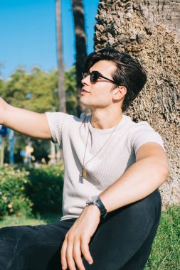 Modayı takip eden beyaz tenli yakışıklı hippi elinde akıllı telefon, parkta selfie çekimi için poz veriyor. Sosyal ağlarda paylaşmak için video çeken genç bir erkek blogcu.