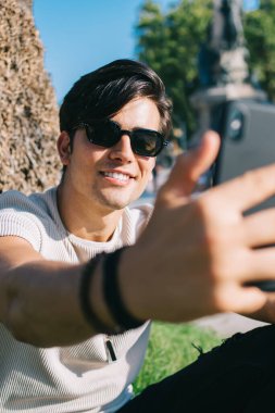 Neşeli 20 'li yaşlarda yakışıklı bir erkek hafta sonları akıllı telefon kamerasıyla selfie çekerek güneşli bir günün tadını çıkarıyor ve cep telefonunda video çekmek için uygulama kullanıyor.