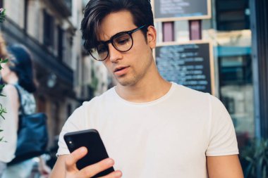 Kafkasyalı ciddi bir beyaz erkek, kafeterya terasında uzaktan çalışırken cep telefonuyla gelir mesajlarını kontrol ediyor. Düşünceli, zengin bir adam blogcusu, internet sitesinde medyayı paylaşmak için modern teknolojileri kullanıyor.