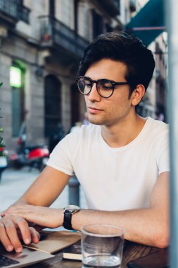 Görme korumalı gözlüklü başarılı beyaz erkek blogcu Laptop bilgisayarında uzaktan çalışıyor yakışıklı esmer hippi öğrenci kafe terasında eğitim videosu izliyor.