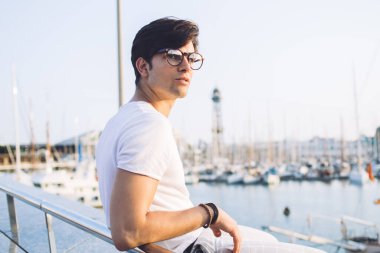 Marina limanında dinlenen, gözlerini kaçıran, yaz tatillerini hayal eden, şık kıyafetli, şık giyinmiş, 20 'li yaşlarda, deniz koyunda boş vakit geçiren beyaz bir erkek.