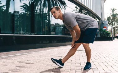 Güçlü beyaz erkek koşucu ısınma egzersizleri yapıyor. Sokaklarda kaslarını esnetiyor, sporcu aktif olarak antrenman yapıyor. Sağlıklı yaşam tarzını, yaşam tarzını ve sağlığını korumaya odaklanıyor.