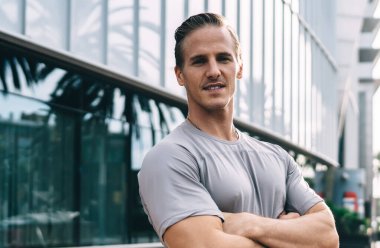 Şehirdeki etkinlik arasında kameraya bakan beyaz erkek sporcunun yarı boyunda portresi. Çapraz pozlar veren kararlı sporcu çapraz forma için şehir sokaklarında zaman harcıyor.