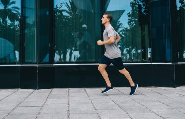 Kentteki kardiyo eğitimi sırasında koşan kararlı erkek koşucunun yandan görünüşü, fiziksel yoğunluk üzerinde yoğunlaşmak için ısınma sırasında dayanıklılık egzersizi yapan beyaz bir adam.