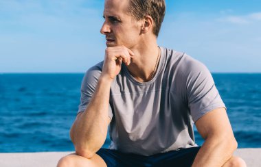 Düşünceli beyaz erkek koşucu. 30 yaşında. Su dolu barajda dinleniyor. Aktif giyinen aktif sporcu antrenmanı bitirmeyi düşünüyor.