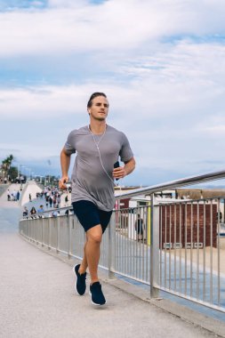 Beyaz tenli vücut geliştirici, enerji elde etmek için boş zamanların tadını çıkarıyor. Elektronik kulaklıklı erkek sporcu, sabah antrenmanında koşuyor, sağlığını ve canlılığını koruyor.