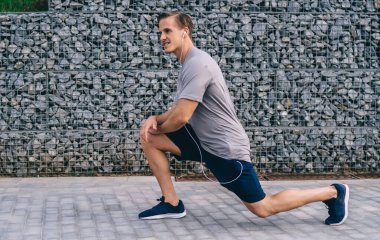 Antrenman sırasında çömelme hareketleri yapan güçlü erkek atlet ve caddede alt vücut kasları? Yaşamsal enerji elde etmek için ısınma egzersizleri yaparak formda kalan aucasian sporcusu