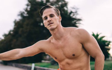 Güçlü erkek antrenör. 20 'li yaşlarda. Sabah antrenmanı sırasında vücut kaslarını esnetiyor. Karın kasları şişmiş üstsüz sporcu.