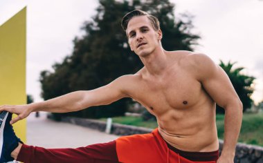 Güçlü erkek antrenör. 20 'li yaşlarda. Sabah antrenmanı sırasında vücut kaslarını esnetiyor. Karın kasları şişmiş üstsüz sporcu.