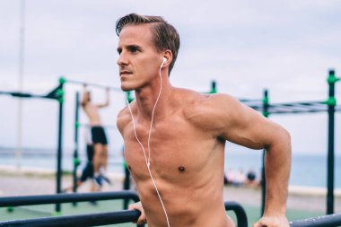 Beyaz tenli güçlü sporcu açık hava barlarında egzersiz yapıyor elektronik kulaklıkla müzik dinliyor ve sağlıklı yaşam tarzını koruyor üstsüz erkek vücut geliştirici vücut kaslarını ve vücut şeklini eğitiyor.