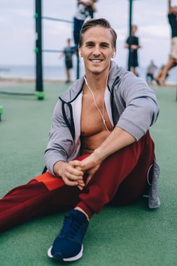 Dijital kulaklıklı neşeli erkek çalıştırıcının portresi. Pozitif motivasyon müziği dinliyor ve kameraya gülümsüyor. Beyazlı mutlu adam spor sahasında canlılık ve antrenman zamanından memnun.