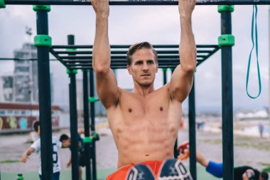 Beyaz tenli erkek atlet gövde ve pazılarını spor sahasında parmaklık kullanarak çalıştırıyor. Güç ve canlılık hissediyor. Mükemmel vücut şeklini korumak için egzersiz yapıyor.