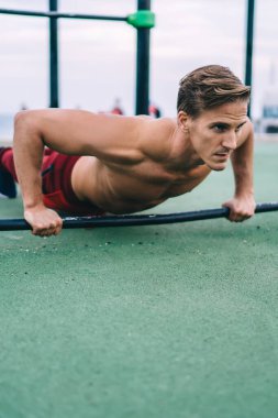 Spor salonundaki parmaklıklardan yukarı iten kaslı elleri olan genç beyaz erkek ısınmak için ekipman kullanıyor, spor tişörtsüz adam mükemmel vücut şeklini korumak için aktif egzersiz yapıyor.