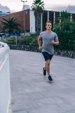 Aktif giyimde yakışıklı beyaz erkek koşucu şehir merkezlerinde sabah antrenmanı yapıyor, hedeflere ulaşıyor, şehirde kardiyo eğitimi alan kararlı sporcu vücut şeklini maratona hazırlıyor.