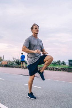 Kafkasyalı erkek koşucu hareketli, ısınan bacak kasları caddede zıplıyor, canlılık ve fiziksel güçten tatmin oluyor, hipster adam boş zamanını dışarıda antrenman yaparak geçiriyor.