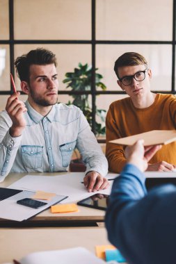 Ciddi bir grup genç erkek tasarımcı modern ofiste birlikte çalışıyor. Kafkasyalı bir adam, öndeki meslektaşlarına evrak veriyor. İşbirliği ve işbirliği kavramı.