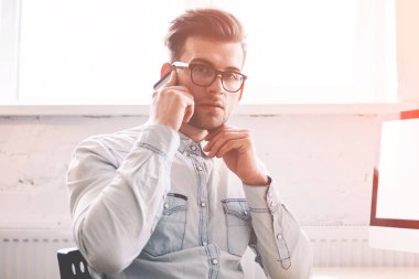 Özgüvenli erkek programcı, arka planda internet reklamınız için boş ekranlı bir evde otururken kameraya bakarak hesap bakiyesini kontrol etmek için operatörle konuşuyor.