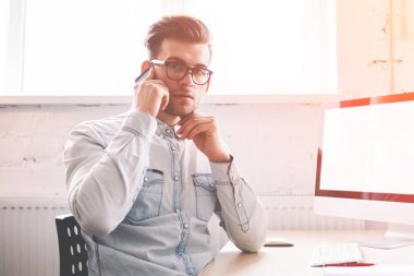 Özgüvenli erkek programcı, arka planda internet reklamınız için boş ekranlı bir evde otururken kameraya bakarak hesap bakiyesini kontrol etmek için operatörle konuşuyor.