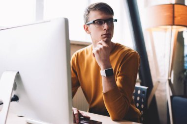 Kafkasyalı hippi, bilgisayardaki kablosuz bağlantıyı kuruyor. Ofis bilgisayarında kalıyor. Gözlüklü genç adam, modern teknolojiye uygulama yüklerken başka yöne bakıyor.