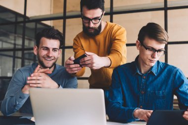 Millennial hipster 'lı gençler birlikte çalışarak bilgisayar ekranının fotoğraflarını çekerken, bilgisayarlı tablet üzerinden SMS mesajları okurken bilgisayarla aynı masada oturuyorlar.