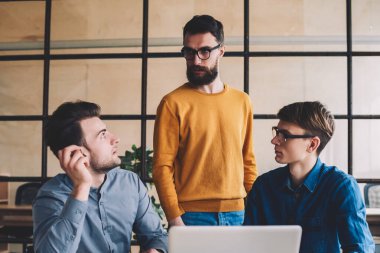 Dizüstü bilgisayar ve çevrimiçi uygulama işbirliği yaparak yeni bir proje için fikir alışverişinde bulunan yetenekli erkek meslektaşlar, ofiste çalışırken birbirleriyle konuşan bir grup genç.