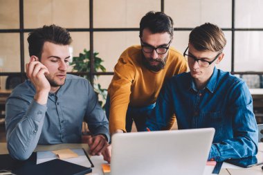 Modern dizüstü bilgisayarda online uygulama üzerinden internetten interneti izleyen bir grup genç erkek iş arkadaşı, yeni başlatılan proje için internet üzerinde araştırma yapan yetenekli adamlar.