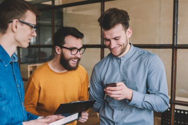 Mutlu erkek arkadaşlar uygulama üzerinden cep telefonuyla sohbet mesajları okuyor, genç adam akıllı telefon cihazında kablosuz interneti kullanarak iş arkadaşlarıyla komik videolar izliyor.