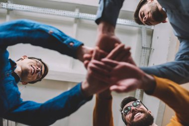 Bir grup başarılı erkek partner kazanmayı ve el ele tutuşmayı kutluyor. Bir grup erkek el birliği ve takım çalışmasını kapalı mekanda gösteriyor. İşbirliği ve katılım kavramı.