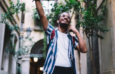 Pozitif Afro-Amerikan hipster melodisi kulaklıklarda mükemmel bir sesle heyecanlanan, şehirde müzik eşliğinde dans eden, cep telefonu çalma listesindeki yeni şarkılarla tatmin olmuş koyu tenli bir erkek.