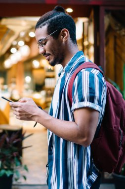 Gülümseyen koyu tenli erkek gezgin akıllı telefonuyla geziniyor. Navigasyon uygulamasını kullanıyor, varış noktalarını ve kafeleri arıyor. 20 'li yaşlarda Afro-Amerikan hipster bir adam şehir merkezinde gezinirken sohbet ediyor.