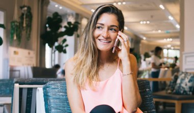 Modern kafede rahat koltukta oturan, akıllı telefondan konuşan ve gözlerini kaçıran, gündelik İspanyol kadın.