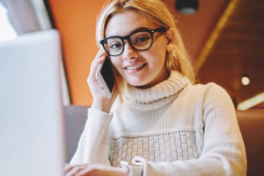 Bilgisayarda online kurs öğrenirken telefon görüşmesi yapan neşeli sevimli bir öğrencinin portresi, cep telefonunda uzaktan çalışan iş hakkında konuşan, gülümseyen bir serbest kadın.