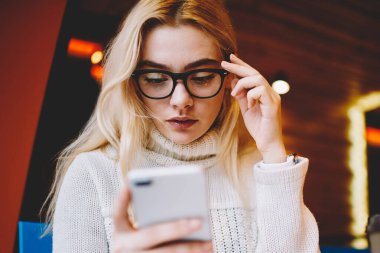 Kafedeki akıllı telefon uygulaması aracılığıyla bankacılık bakiyesini kontrol eden düşünceli genç bir kadın, telefondaki faturayla ilgili konsantre kadın okuma bildirimi işlem yapmak için internet uygulaması kullanıyor