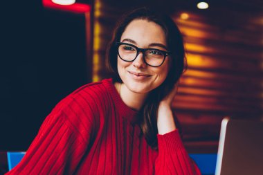 Gülümseyen genç bir kadın kafenin içinde serbest çalışmaktan zevk alıyor not defterindeki fikirleri not alıyor. Pozitif kız öğrenci ödevlerini iyi bir şekilde yapıyor. Laptop bilgisayarından öğrendiği için kablosuz internetten memnun.