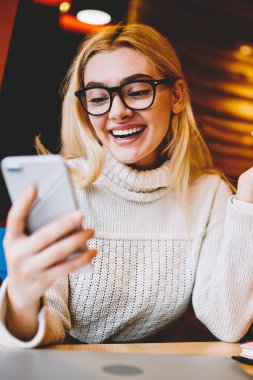 Neşeli hippi kız akıllı telefondan gelen iyi haberlerle heyecanlanıyor kafeteryada oturuyor, duygusal kadın internet iletişimi için indirimden memnun. Haberleri telefonla kontrol ediyor.