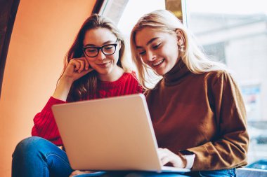 Pozitif kız öğrenci eğitim webinar birlikte kablosuz bağlantı ve dizüstü bilgisayar kullanarak coworking uzayda genç kız arkadaşlar eğlenmeye izlerken zevk netbook üzerinde boş zaman üzerinde ağ