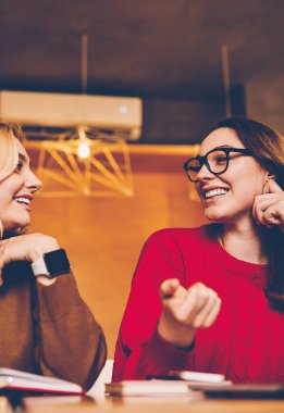 Başarılı serbest iş hakkında iletişim kuran mutlu genç kadınlar kafeteryada uzaktan çalışıyor, neşeli hippi kızlar ev ödevlerini yaparken birbirleriyle arkadaşça konuşmaktan zevk alıyorlar.