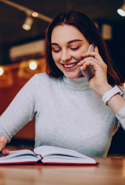 Telefon görüşmesi tamamlanmış kurs hakkında good news paylaşmak için genç hippi kız gülümseyerek, ödev yazma ve Smartphone'da arkadaşla konuşurken mutlu genç kadını tatmin ile tarifeleri