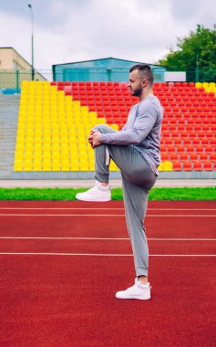 Aktif giyimli ve spor ayakkabılı formalı genç sporcunun şehir stadyumunda antrenman yaparken bacak kaslarını ısıtması.